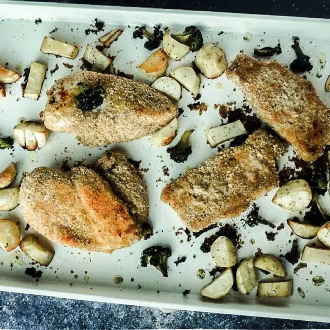 Shake and bake chicken and pork on a sheet pan with a dark backdrop. Veggies surround it.