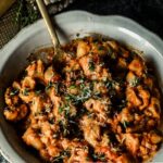 Slow Cooker Hamburger Helper in a white scalloped dish with Italian Greens sprinkled on top. A gold spoon and wedge of parmesan are to the left.