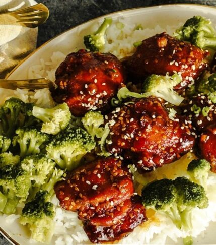 Sweet and Spicy Teriyaki Chicken on a bed of rice with broccoli and sesame seeds sprinkled on top. Gold tongs rest to the left.