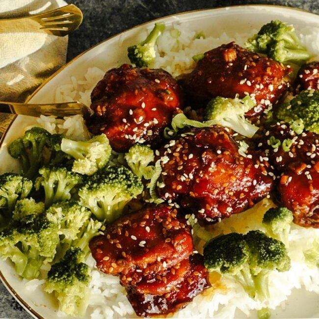 Sweet and Spicy Teriyaki Chicken on a bed of rice with broccoli and sesame seeds sprinkled on top. Gold tongs rest to the left.