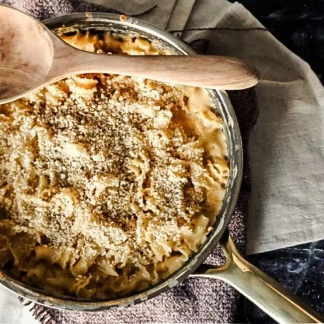 Baked Macaroni and Cheese with Bread Crumbs on Top in a skillet. A black back drop with off white tea towels