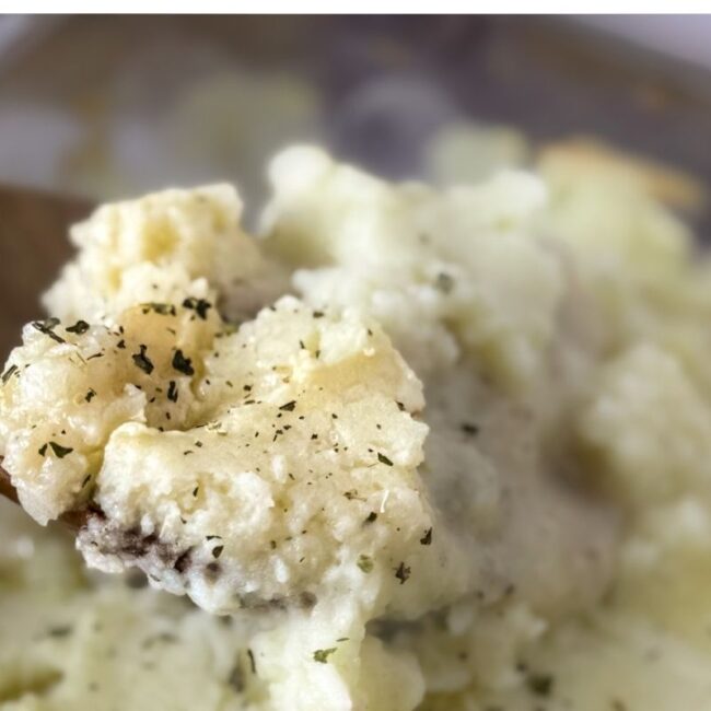 A scoop of chicken and mashed potato bake with a wooden spoon over the casserole.