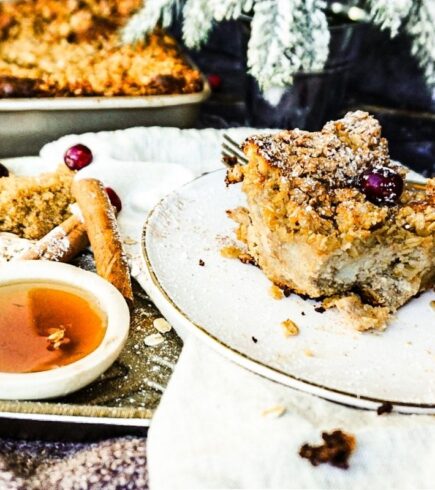 Gingerbread French Toast Bake on a white plate with syrup, on the side, cinnamon stick, a fork and dark background.