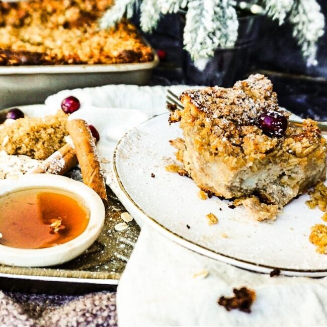 Gingerbread French Toast Bake on a white plate with syrup, on the side, cinnamon stick, a fork and dark background.
