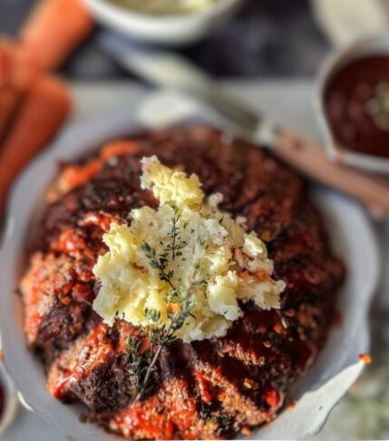 Holiday meatloaf with mashed potatoes in the middle. Carrots are to the top left, ketchup to the top right and a white backdrop.
