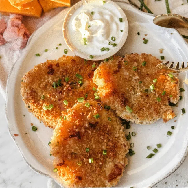 3 panko breakfast bites on a white plate with cheese and ham in the background.