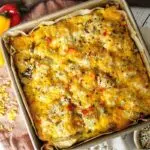 Sausage Breakfast bake in a square baking dish with a white back drop and dish towel behind. Cheese grater to the left with peppers.