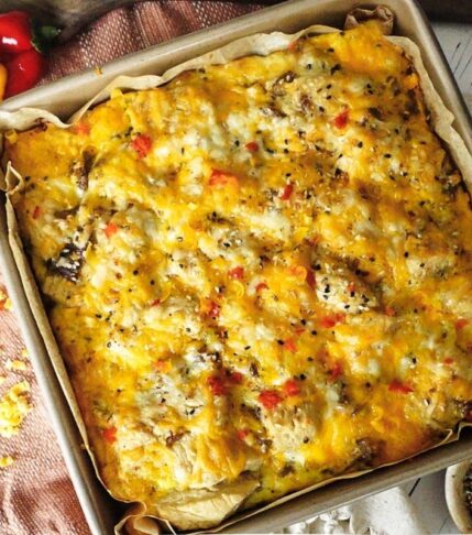 Sausage Breakfast bake in a square baking dish with a white back drop and dish towel behind. Cheese grater to the left with peppers.