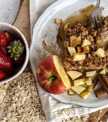 Apple Spice Oatmeal on a plate with apples on top. Strawberries in a small bowl to the left with oats underneath.