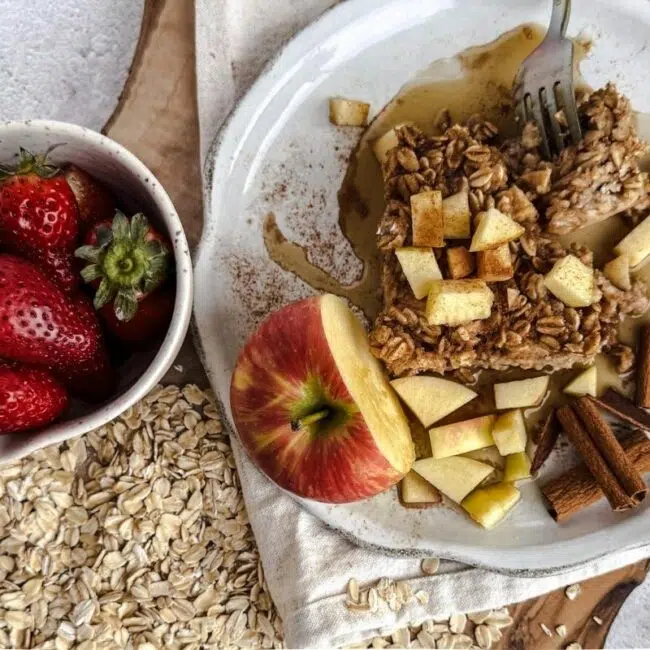 Apple Spice Oatmeal on a plate with apples on top. Strawberries in a small bowl to the left with oats underneath.