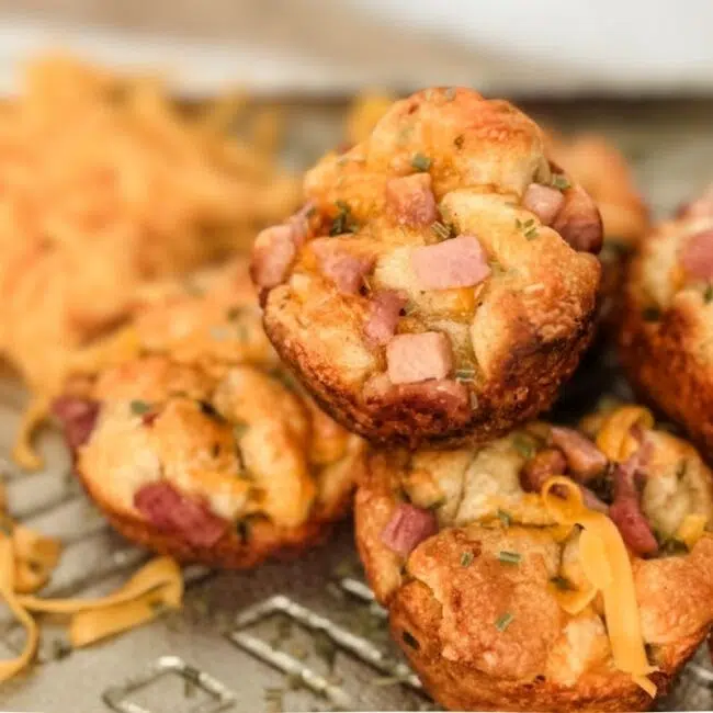 A stack of garlic cheddar bombs with cheddar cheese to the top left. There is a shiny gold back drop.