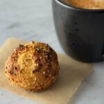 Everything bagel bomb filled with cream cheese on a piece of parchment paper with a coffee mug in the background.