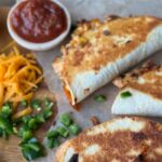 Crispy Chicken Tacos with a wooden backdrop and parchment paper. Sprinkled with Jalapenos and cheese. Dipping sauce sits to the left.