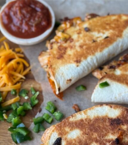 Crispy Chicken Tacos with a wooden backdrop and parchment paper. Sprinkled with Jalapenos and cheese. Dipping sauce sits to the left.