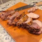 Pork loin cut on a cutting board. A knife is in the background on its side.